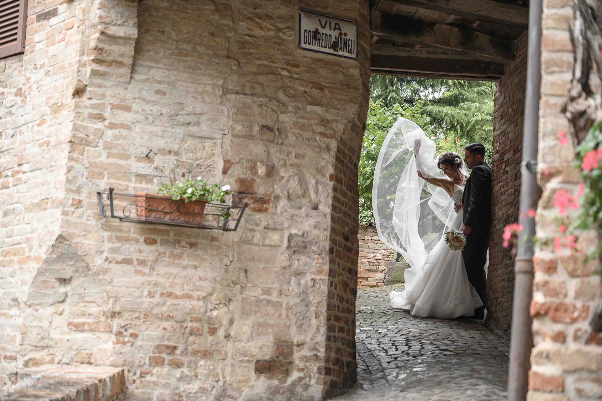 servizio fotografico sposi appoggiati al muro mentre la sposa tira su il velo trasparente
